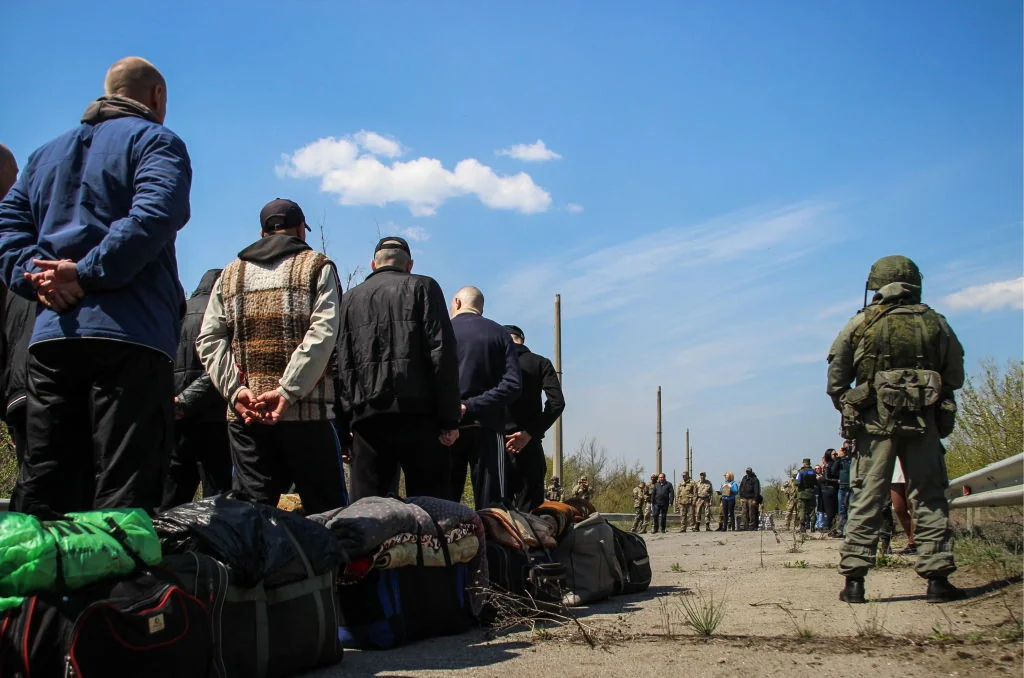 Цивільні заручники України зі багажем під наглядом військового на блокпосту