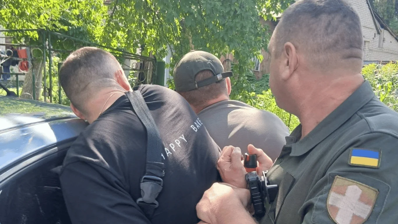 Військовий з шевроном України затримує чоловіка в чорній футболці біля авто