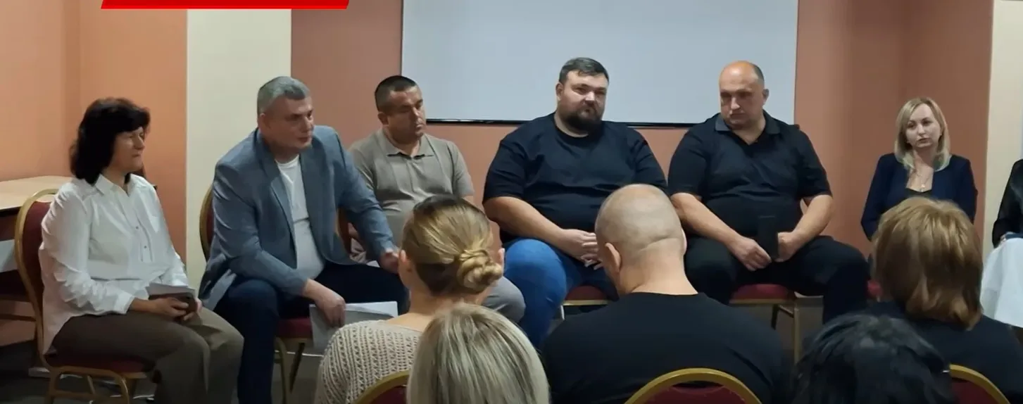 Учасники сидять у колі в залі з екраном на нараді