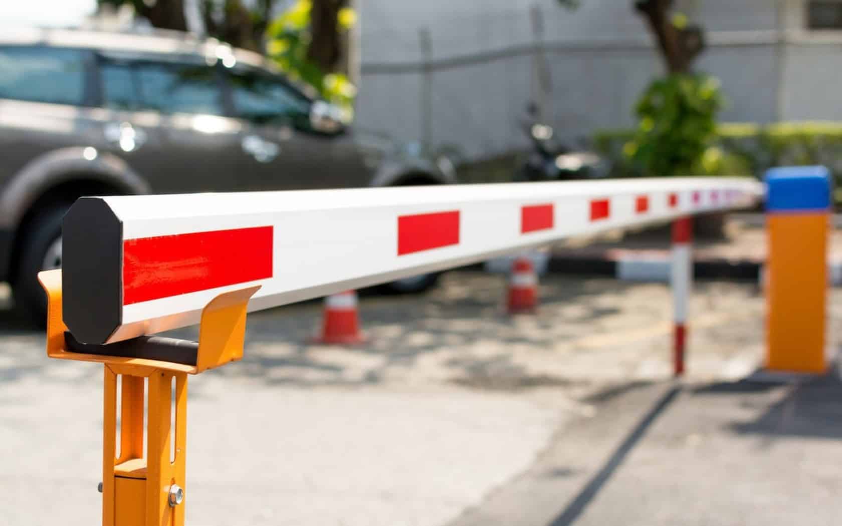 Білий шлагбаум із червоними смугами на жовтому стовпі біля авто