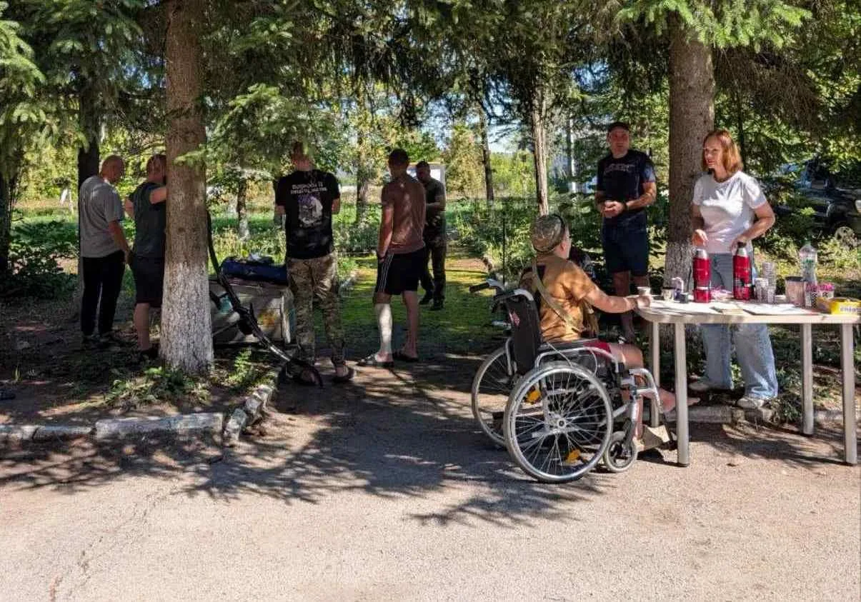 Люди під ялинками біля столу, учасник у візку і лук біля спорядження